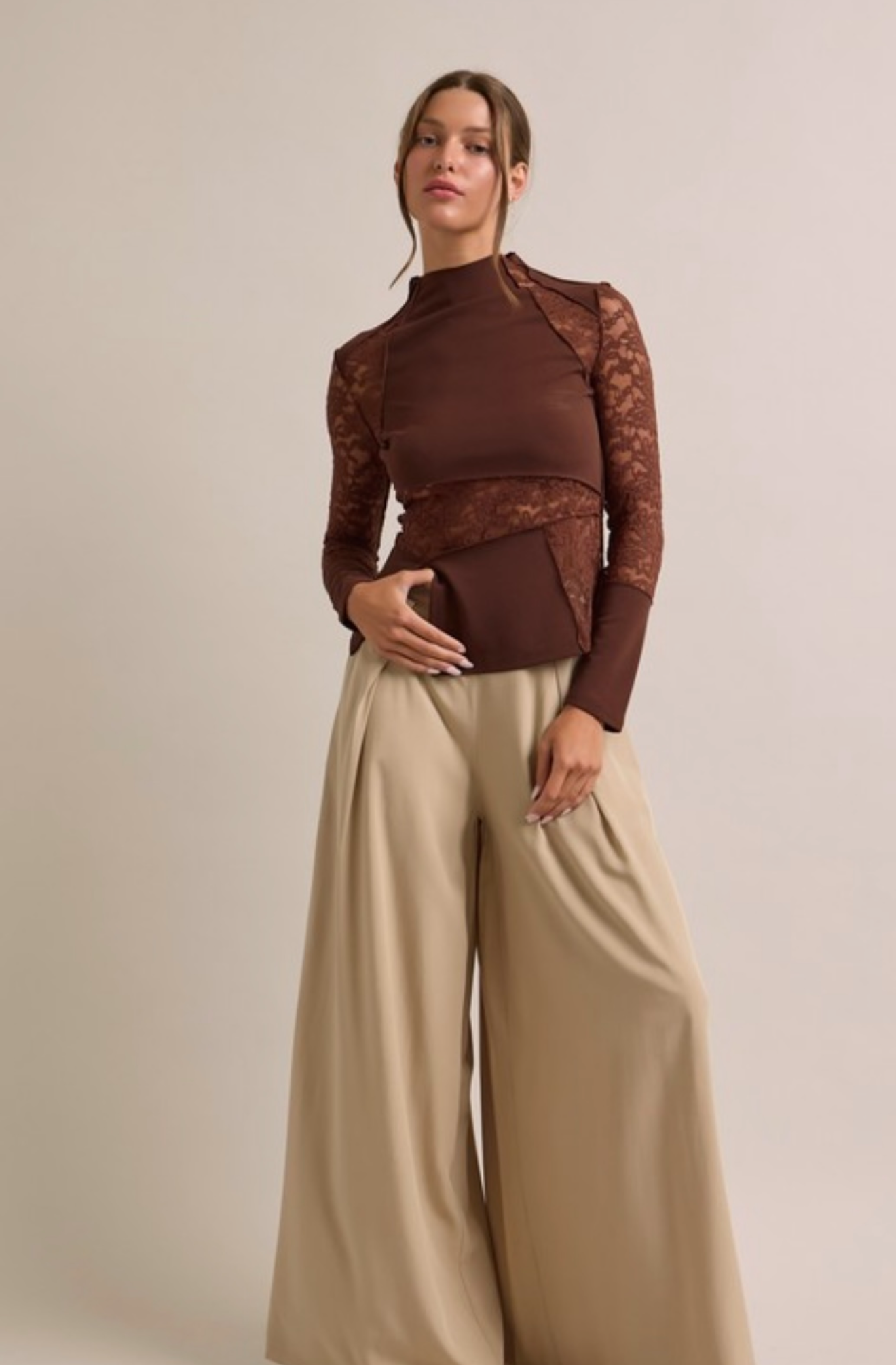 Woman wearing a brown top with lace details and beige wide-leg pants against a plain background
