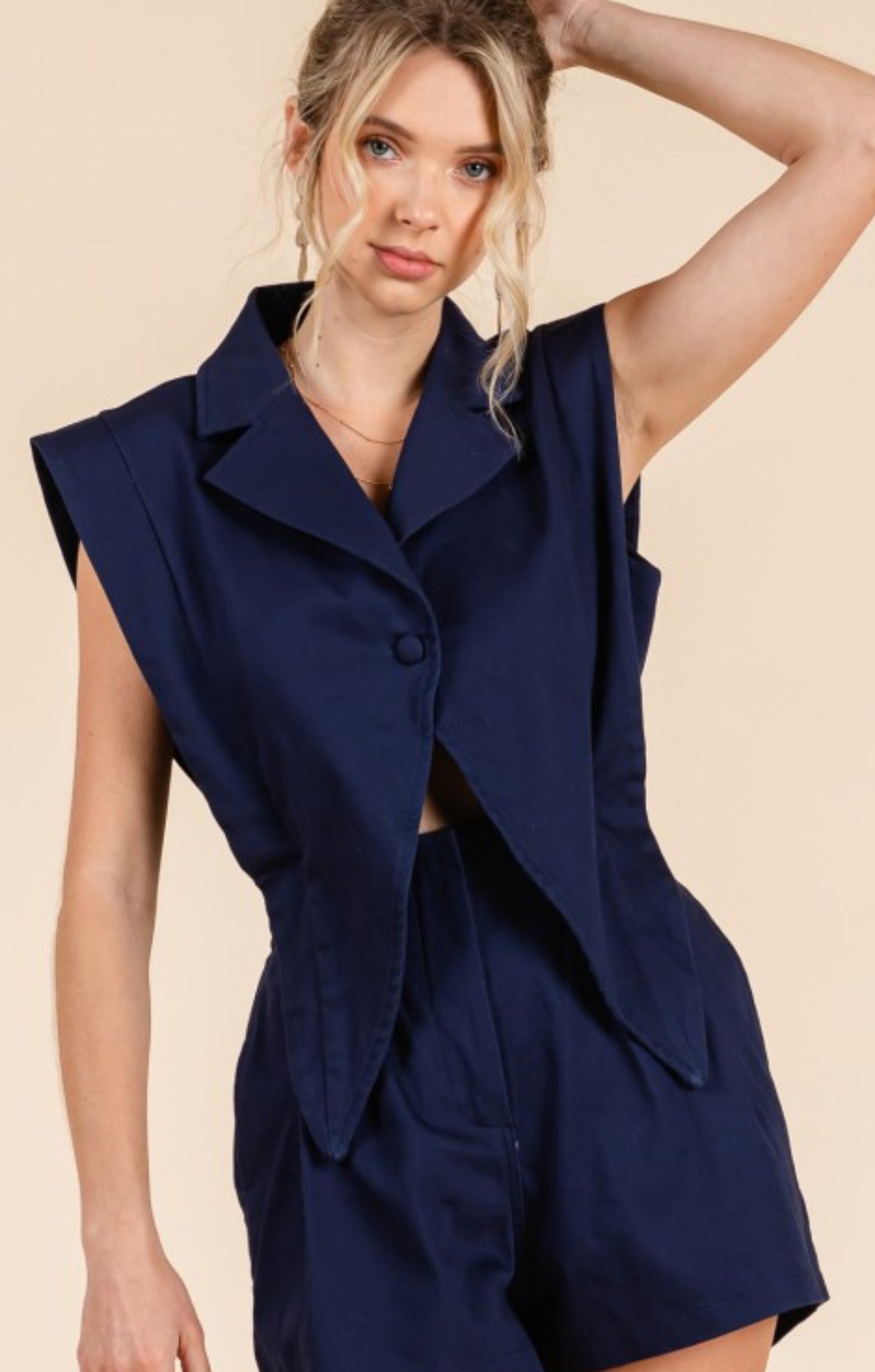 Woman wearing a navy blue sleeveless blazer and shorts set on a beige background