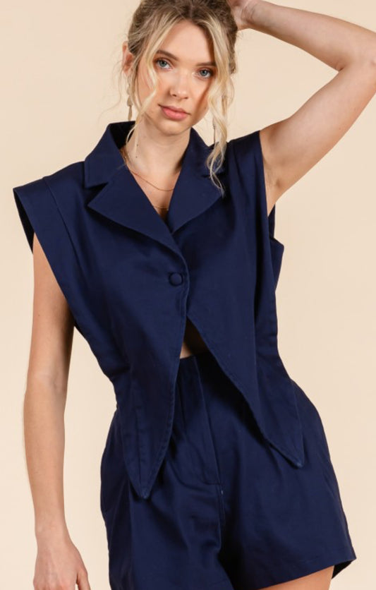 Woman wearing a navy blue sleeveless blazer and shorts set on a beige background