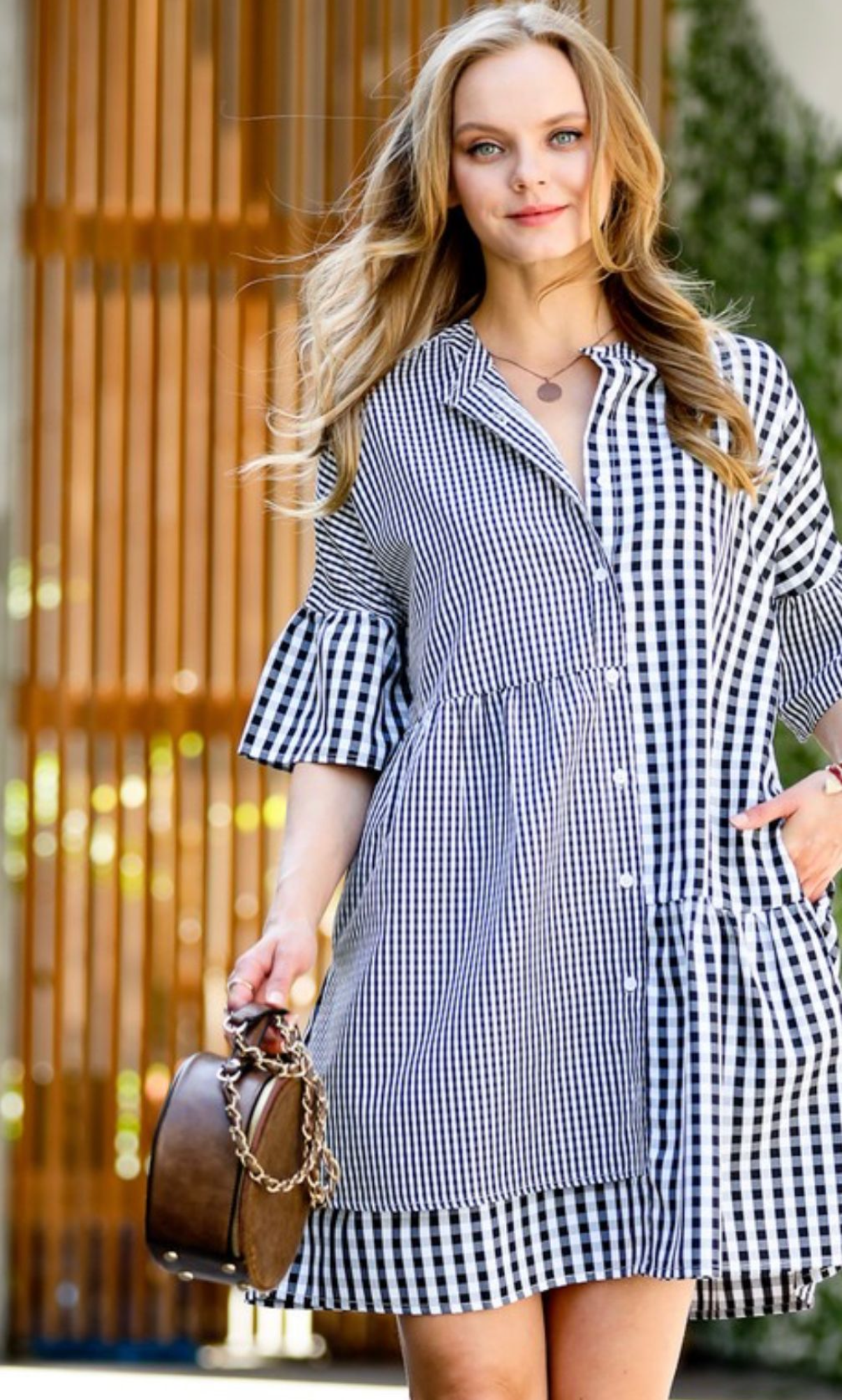 Woman wearing a blue and white checkered dress holding a brown handbag.
